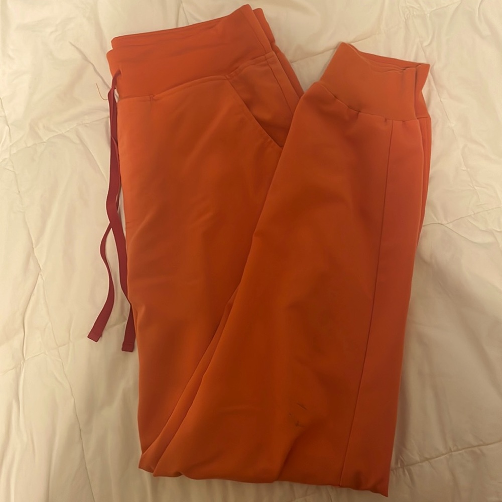 Medium tall sunset orange Zamora scrub jogger. Medium wear, some ink stains